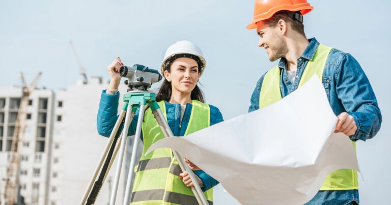 Eine Frau und ein Mann in Leuchtwesten machen Abmessungen auf einer Baustelle.
