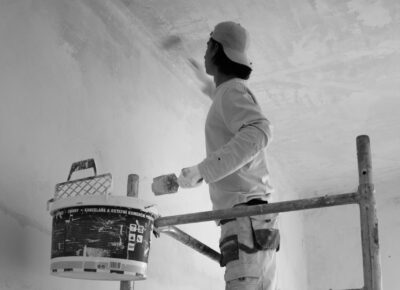 fassadenfarbe richtig wählen, Maler trägt Farbe mit Rolle auf verputzten Untergrund auf