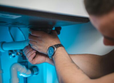 Sanitärinstallateur überprüft Leitungen unter einem Lavabo