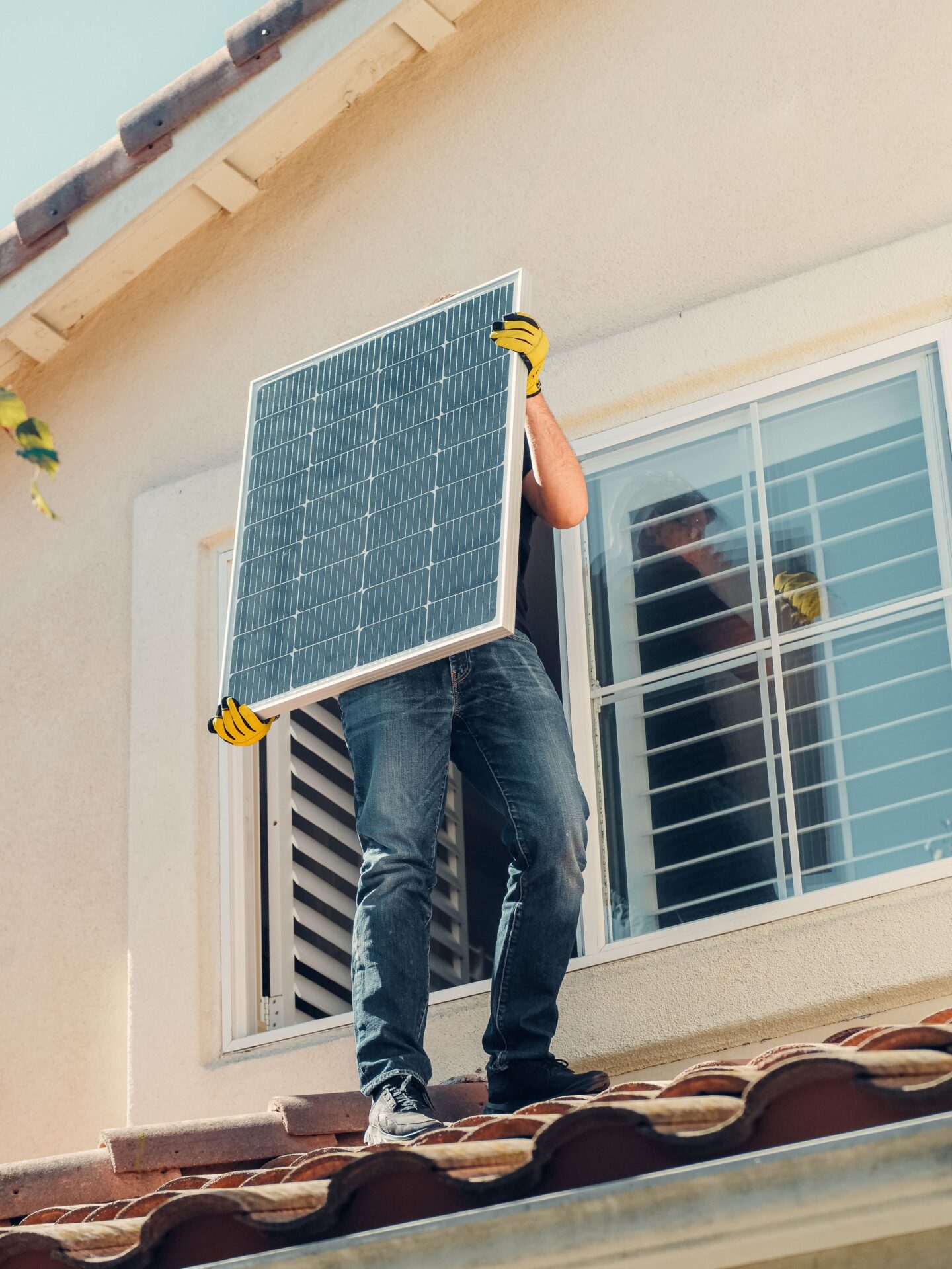 Person mit Solarmodul auf dem Dach eines Wohnhauses