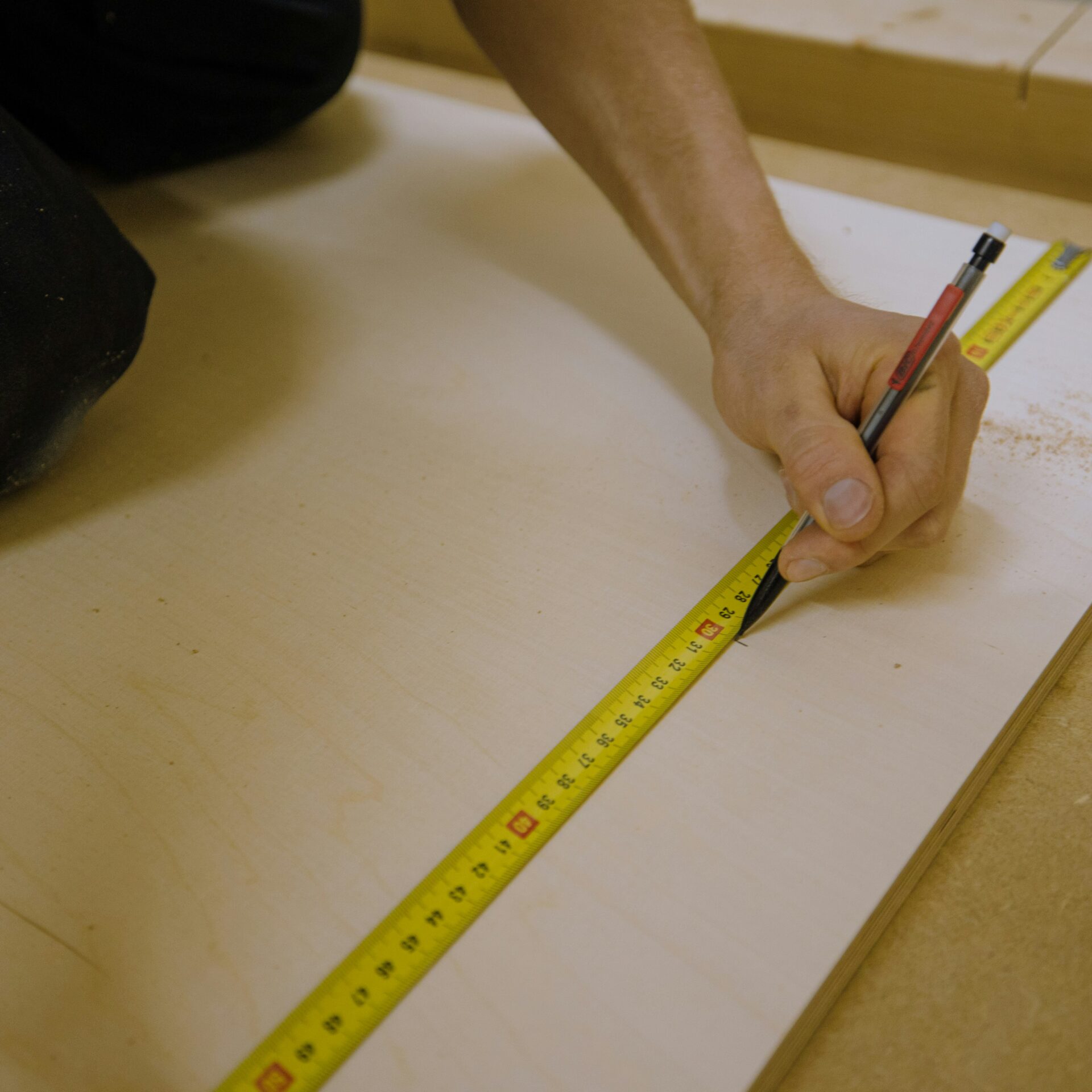 Handwerker misst eine Holzplatte mit einem Massstab aus