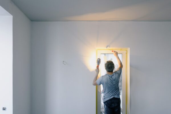Mann streicht mit einer Farbrolle eine Innenwand neben einem Fenster