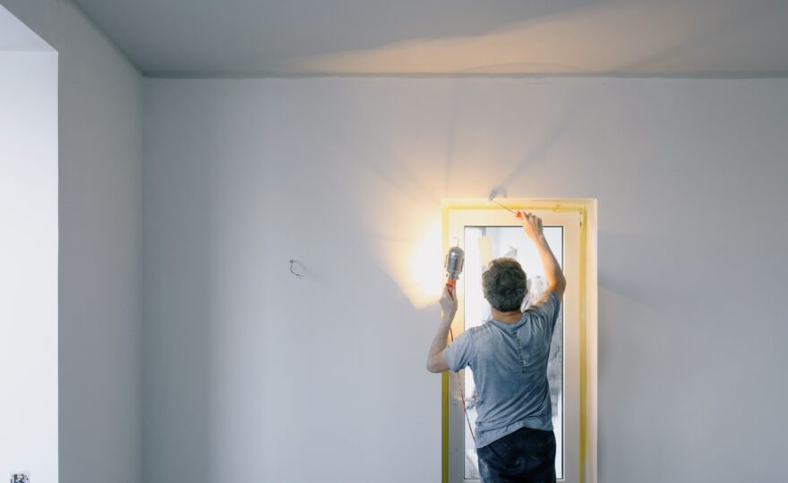 Mann streicht mit einer Farbrolle eine Innenwand neben einem Fenster